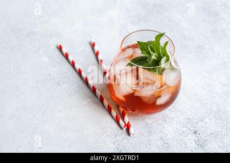 From above refreshing glass of Coke cocktail garnished with fresh mint leaves and served with striped red and white straws, set on a textured gray sur Stock Photo