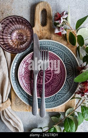 Top view image captures a beautiful table setting featuring a rustic wood cutting board, textured ceramic plates in shades of purple and blue, complem Stock Photo