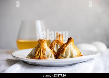 Authentic Georgian khinkali dumplings served on a white plate, expertly cooked A clear glass of white wine complements the scene, heightening the culi Stock Photo