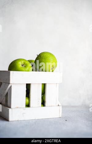 A collection of ripe green apples are neatly arranged in a white wooden crate, set against a soft gray background, invoking a fresh and organic feel Stock Photo