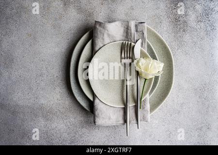 Top view of tasteful table setting featuring a stack of neutral colored plates, a neatly folded gray linen napkin, and stainless steel cutlery, adorne Stock Photo