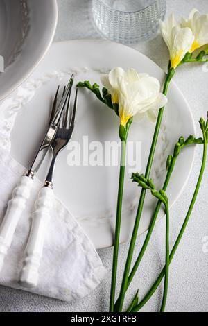 A sophisticated table setting featuring white porcelain plates, silver cutlery with white handles, a linen napkin, and fresh white freesias as centerp Stock Photo