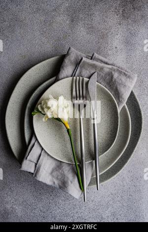 This image showcases a sophisticated table setting featuring a fresh freesia flower on speckled ceramic plates, complemented by sleek silverware and a Stock Photo