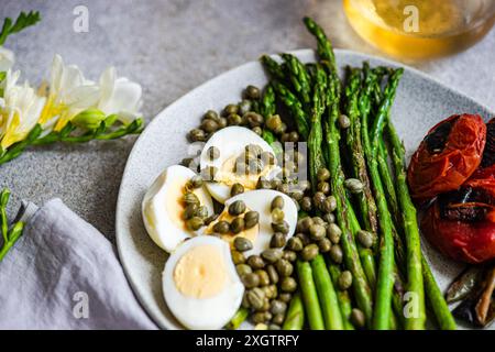 A nutritious meal featuring boiled eggs, barbecued asparagus, capers, and grilled vegetables including tomatoes and chili peppers, artistically arrang Stock Photo