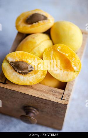 Bright yellow nectarines, both whole and halved, are neatly arranged in a rustic wooden drawer, displaying their vibrant, juicy flesh and central pits Stock Photo