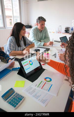 In a well-lit office, a diverse team reviews data on a digital tablet and paper materials The atmosphere is collaborative, with participants engaging Stock Photo