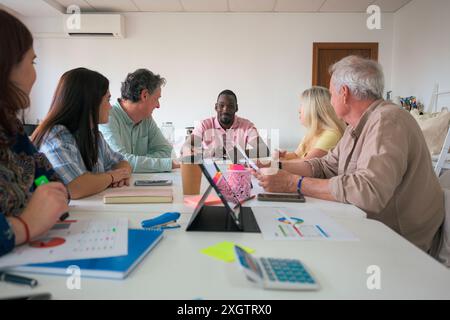 A multiracial group of professionals engaging in a collaborative office meeting They are seated around a white table, discussing over documents and di Stock Photo