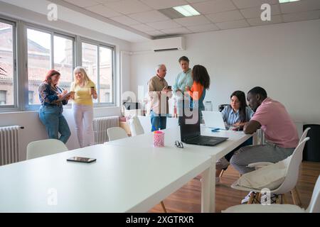 A group of colleagues collaboratively working and discussing in a well-lit office space The image captures men and women of different ages and ethnic Stock Photo