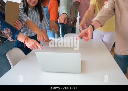 A diverse group of professionals gather around a laptop on a white table, pointing and collaborating in a bright office setting Stock Photo