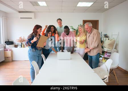 A joyful group of seven diverse individuals celebrates a successful project in a bright, contemporary office The team, displaying excitement and camar Stock Photo