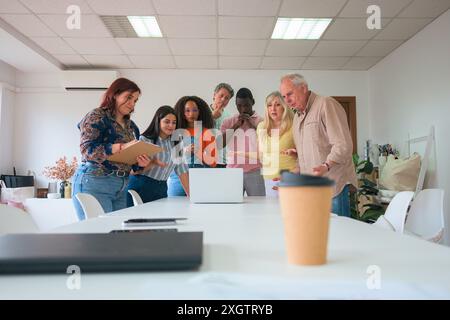 A diverse group of business professionals actively discuss documents and brainstorm ideas around a white table in a well-lit, contemporary office sett Stock Photo