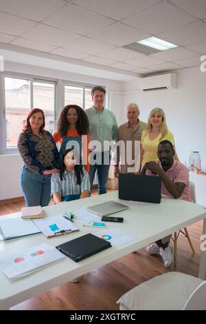 A professional and diverse team stands confidently in a well-lit office space, surrounded by modern office equipment and documents, demonstrating team Stock Photo