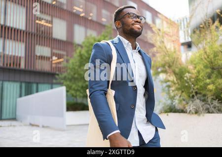 African American businessman in stylish blue suit walks confidently through an urban setting, smiling and looking away from the camera. Stock Photo