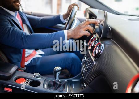 An African American male business professional, dressed in a blue blazer, adjusts the touchscreen of a modern car while smiling. Stock Photo