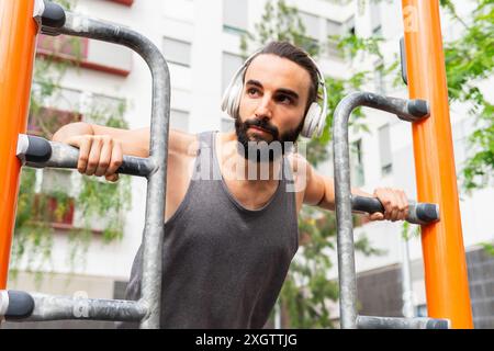 A young adult male works out with headphones on at a public outdoor gym in the Poblenou neighborhood of Barcelona, showcasing a fit lifestyle amid urb Stock Photo