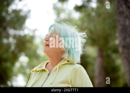 An elderly woman gazes upwards while relaxing outdoors, surrounded by trees. Stock Photo
