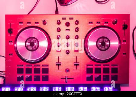 A close-up image of a modern DJ controller bathed in dynamic pink lighting, highlighting its various knobs, buttons, and decks used for mixing music Stock Photo