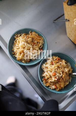 Cropped unrecognizable person view of home-cooked noodle stir-fry with vegetables served in two blue bowls, ready to enjoy Stock Photo