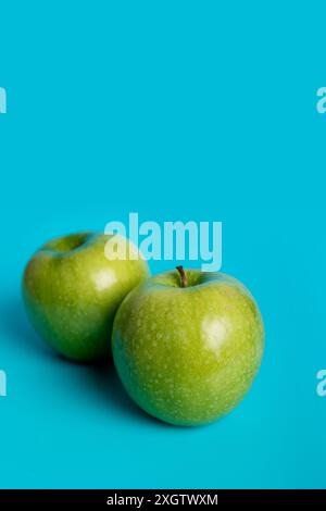 Two vibrant green apples sit against a stark turquoise backdrop, showcasing their glossy texture and natural freshness. This image emphasizes the beau Stock Photo