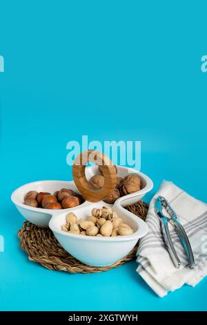 Healthy assorted nuts including walnuts, pistachios, and hazelnuts presented in a segmented bowl on a blue background, enhanced by wooden and wicker t Stock Photo