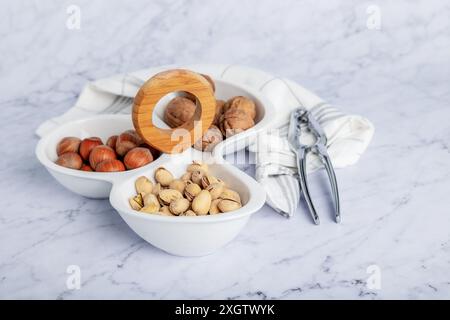 From above marble table setting showcasing a wholesome selection of nuts including walnuts, pistachios, and hazelnuts in white bowls. A wooden nutcrac Stock Photo