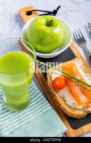 Top view of a nutritious meal with a slice of whole grain toast topped with smoked salmon, cream cheese, and a cherry tomato, accompanied by a fresh g Stock Photo