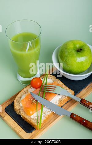 From above nutritious breakfast setup featuring a glass of cucumber and apple juice, a slice of whole grain bread topped with salmon and cream cheese, Stock Photo