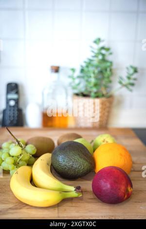Variety of fresh fruits arranged on a wooden kitchen counter. This scene includes bananas, an avocado, a mango, kiwis, grapes, and a mango, softened b Stock Photo