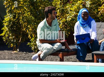 A Caucasian and an African Muslim woman in hijab, engaged in a business discussion outdoors. The man smiles, using a tablet and looking at the camera, Stock Photo