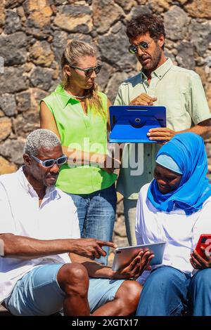 A multiethnic group of four business colleagues engage in a discussion in a sunny outdoor setting. An African American man, a Caucasian woman, an Asia Stock Photo