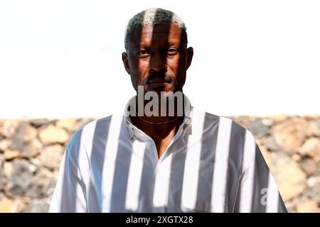 A portrait of a middle-aged Black man wearing a white shirt, standing outdoors. The man is looking at the camera with a calm expression, illuminated b Stock Photo