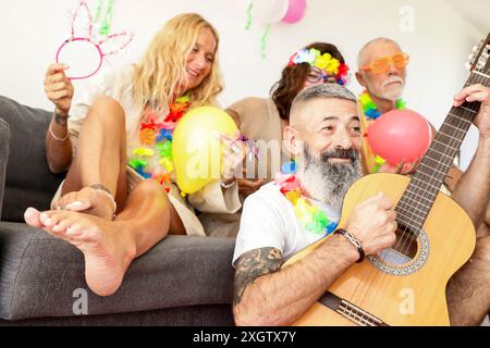 A lively group of adults enjoys a festive gathering. One man plays a guitar while others hold balloons and wear colorful party accessories, creating a Stock Photo
