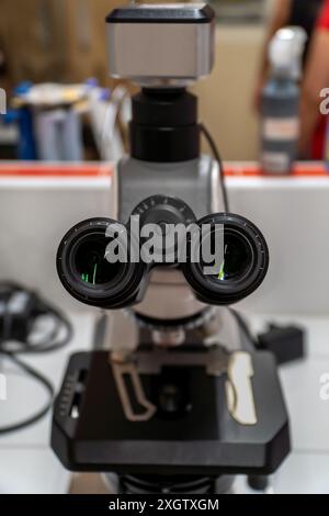 A detailed close-up of a laboratory microscope with dual eyepieces, focused on scientific research and analysis in a cluttered lab setting Stock Photo
