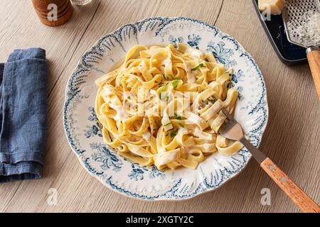 From above, Homemade Italian pasta garnished with fresh parsley and grated Parmesan on a wooden table with pepper mill and cheese grater Stock Photo
