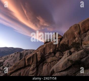 Dramatic sunset clouds cascade over the unique rock formations of La Pedriza, set in the Guadarrama mountains near Madrid Stock Photo