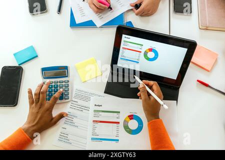 top view of cropped, unrecognizable African American individual engaging in financial analysis using a tablet and various office tools in a brightly l Stock Photo
