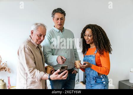 Three diverse coworkers share content on a smartphone in a bright, contemporary coworking space.The African American woman and her two Caucasian colle Stock Photo