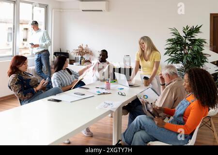 In a brightly lit coworking space, a diverse group of professionals engages in collaborative work. People of varying ages and ethnic backgrounds (Afri Stock Photo