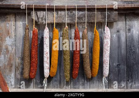 An assortment of vibrant cured sausages including sobrasada, displayed hanging against an aged wooden background, highlighting the rich textures and c Stock Photo