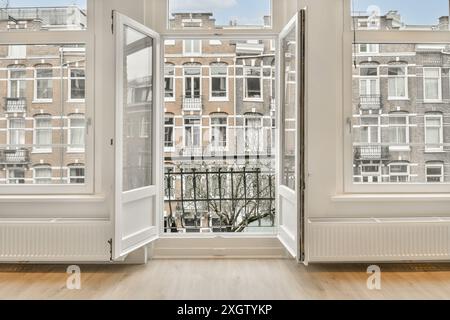 An open window in a room with wooden floors and white trim on the windows, there is a view of buildings Stock Photo