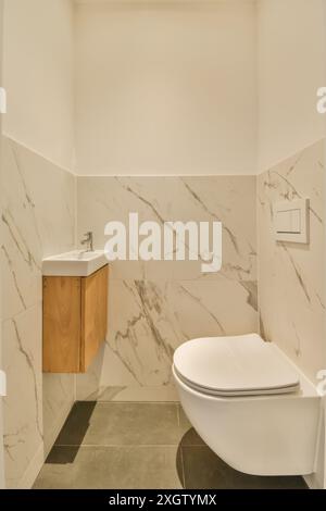 A bathroom with white marble walls and flooring, including a toilet in the middle part of the wall is made out of wood Stock Photo