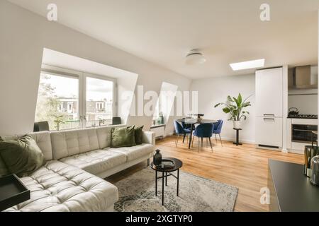 Bright and stylish interior of an apartment showing a combined living room and kitchen with large windows, a plush sofa, and a bold blue dining set at Stock Photo