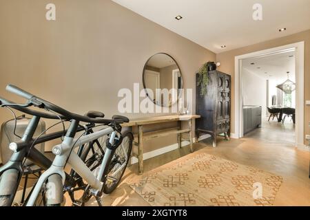 A contemporary hallway interior features bicycles, a rustic wooden table, elegant mirror, and textured rug, blending modernity with vintage elements f Stock Photo