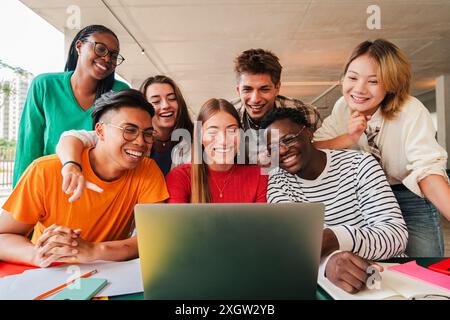 Big group of young students using a laptop to do the homeworks at high school library. Teenagers e-learning with a computer at university campus. Classmates talking and studying for a exam at class. High quality photo Stock Photo