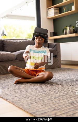 African American boy enjoys virtual reality at home. He's immersed in a VR game, sitting cross-legged on the living room floor. Stock Photo