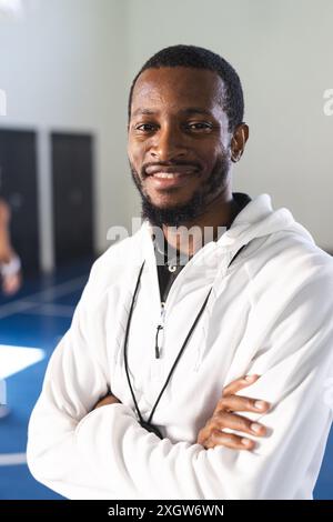 Confident African American basketball coach, embodying both sport and lifestyle, poses at the gym, smiling at the camera. His arms are crossed, showca Stock Photo