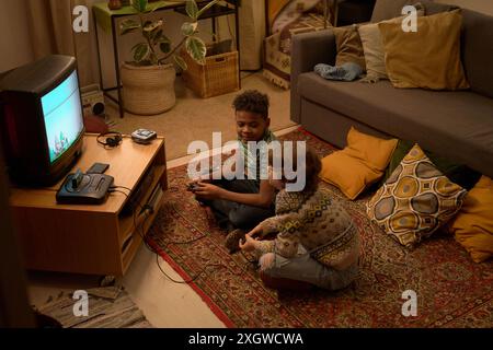 A couple of boys enjoying a retro gaming session, focused on playing retro video game in a cozy living room setting with a mix of modern and vintage decor Stock Photo