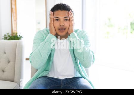Young biracial man looks surprised during a video call at home, with copy space. His expression suggests an unexpected situation or shocking news. Stock Photo