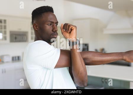 Focused african american man practicing yoga stretching arm at home. Yoga, fitness, domestic life and healthy lifestyle, unaltered. Stock Photo