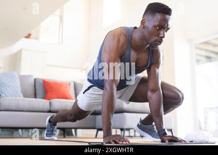 Focused african american man working out on exercise mat at home. Fitness, training, exercise, domestic life and healthy lifestyle, unaltered. Stock Photo